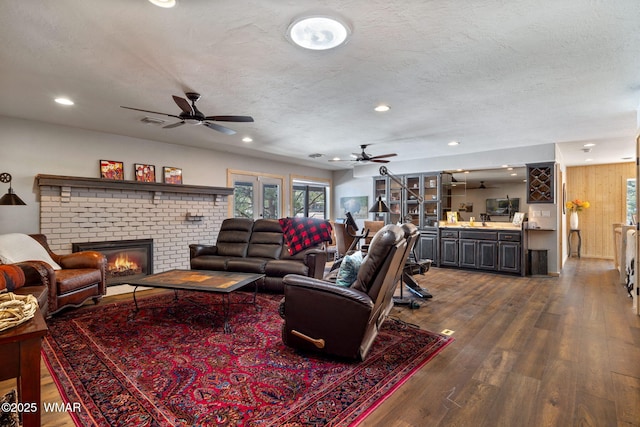 living room with dark wood finished floors, recessed lighting, ceiling fan, a textured ceiling, and a brick fireplace