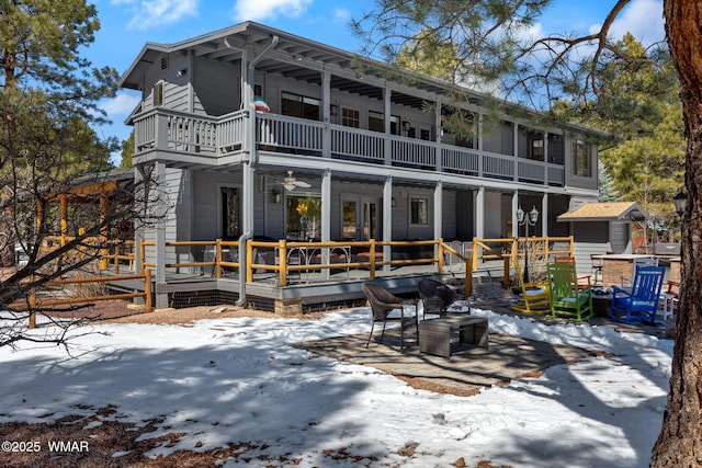 snow covered back of property featuring a balcony and a ceiling fan