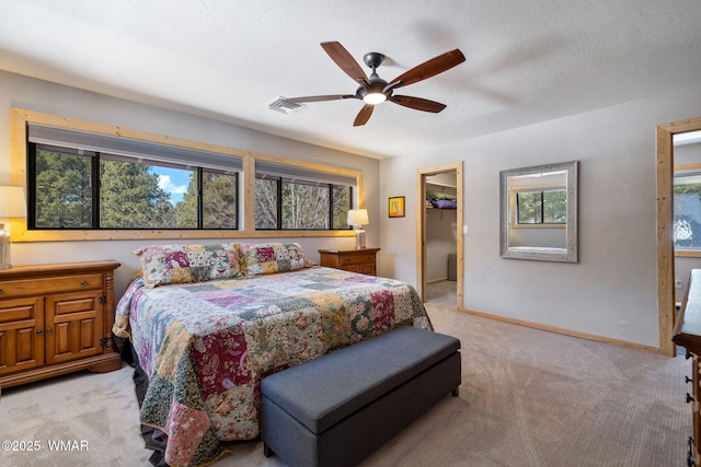 bedroom featuring a spacious closet, visible vents, baseboards, light carpet, and a ceiling fan