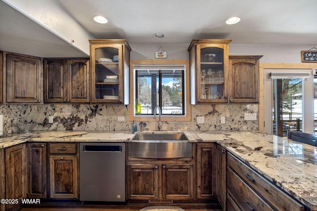 kitchen featuring a sink, backsplash, stainless steel dishwasher, glass insert cabinets, and light stone countertops