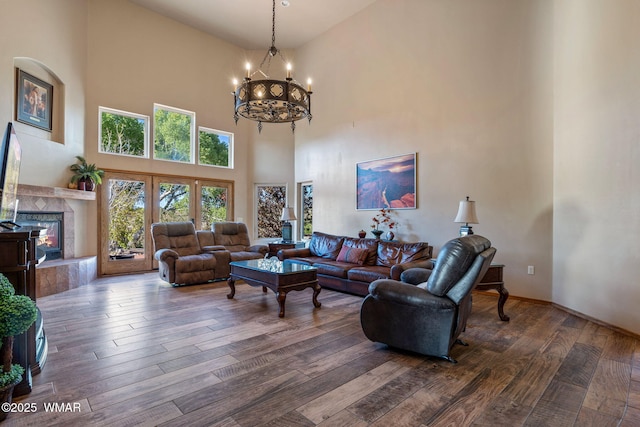 living area with a towering ceiling, hardwood / wood-style flooring, a chandelier, and a tiled fireplace