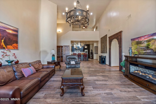 living room featuring a chandelier, a towering ceiling, wood finished floors, a lit fireplace, and arched walkways