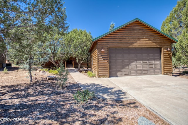 view of front facade featuring a garage, driveway, faux log siding, and an outdoor structure