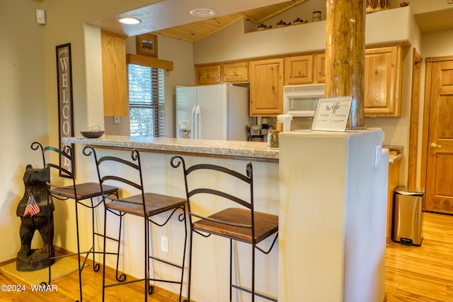 kitchen with light countertops, white appliances, a breakfast bar area, and light brown cabinetry