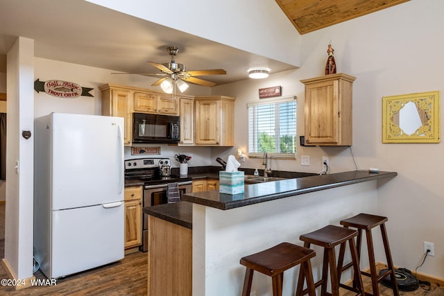 kitchen with freestanding refrigerator, a peninsula, light brown cabinets, black microwave, and a sink