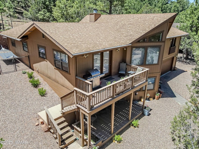 rear view of property featuring a garage, a chimney, a deck, and roof with shingles