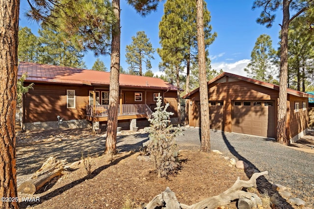 chalet / cabin with a garage, gravel driveway, an outdoor structure, and metal roof