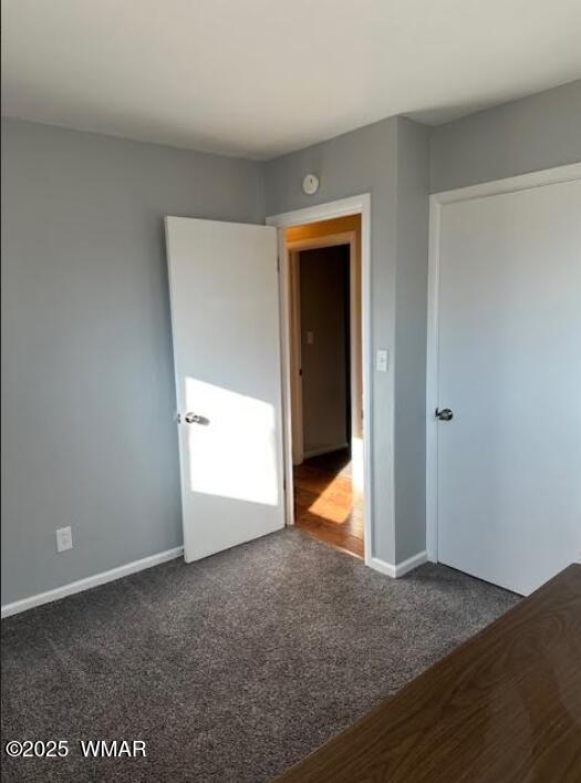 unfurnished bedroom with baseboards and dark colored carpet