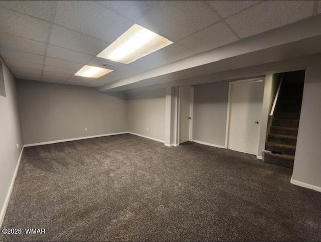 finished below grade area with a paneled ceiling, dark carpet, baseboards, and stairs