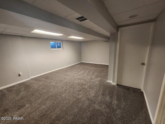 finished below grade area featuring a paneled ceiling, baseboards, visible vents, and dark colored carpet