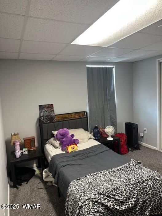 carpeted bedroom featuring a drop ceiling and baseboards