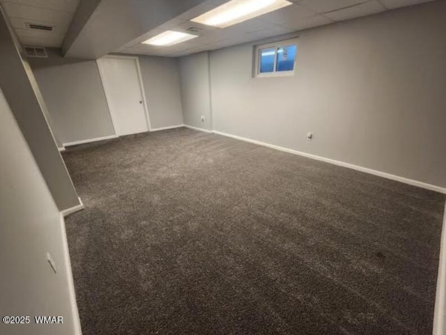 below grade area featuring dark colored carpet, a drop ceiling, and baseboards