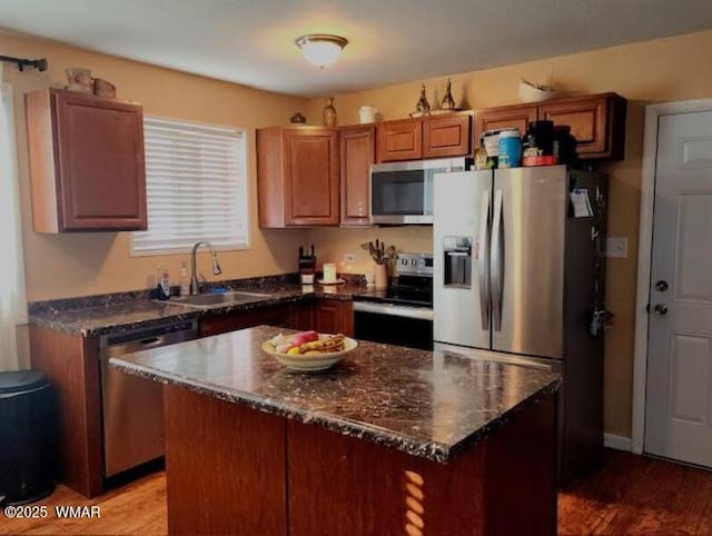 kitchen with stainless steel appliances, wood finished floors, a kitchen island, a sink, and brown cabinets