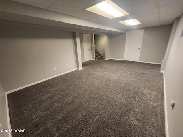 finished basement with a drop ceiling, stairway, dark carpet, and baseboards