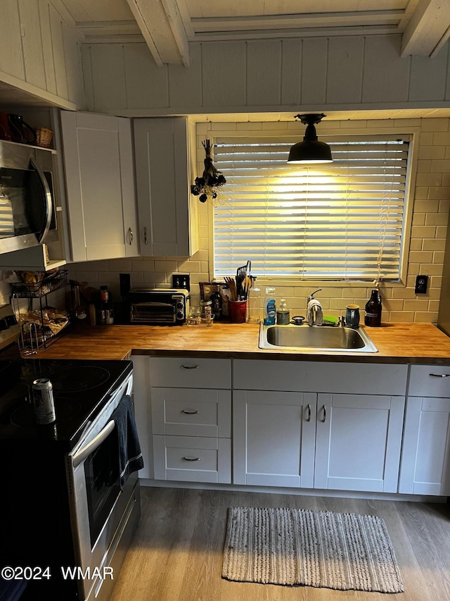 kitchen featuring butcher block countertops, appliances with stainless steel finishes, wood finished floors, white cabinetry, and a sink