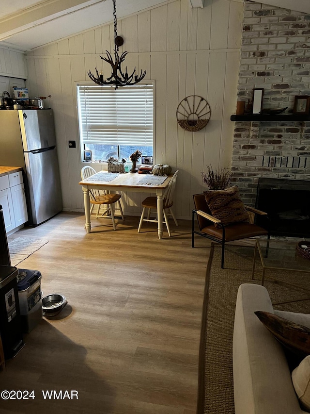 dining space with lofted ceiling, light wood finished floors, a brick fireplace, and a notable chandelier