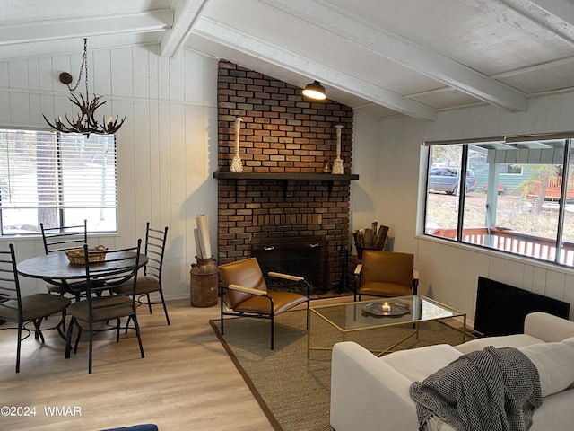 living area with lofted ceiling with beams, light wood-type flooring, a fireplace, and a chandelier