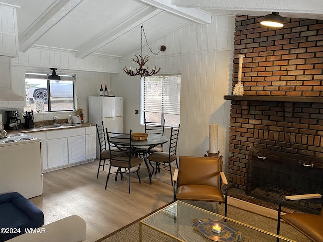 dining area with a brick fireplace, a notable chandelier, lofted ceiling with beams, and light wood finished floors