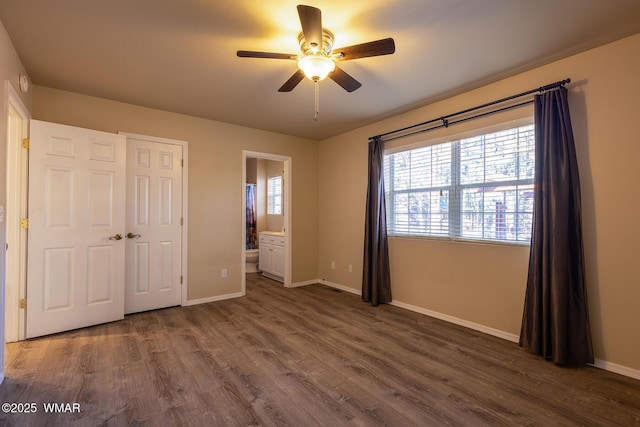 unfurnished bedroom featuring ceiling fan, connected bathroom, baseboards, and dark wood-style flooring