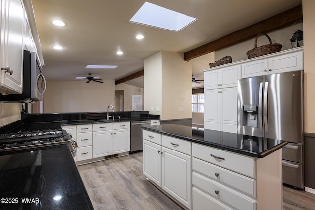 kitchen featuring lofted ceiling with skylight, white cabinetry, stainless steel appliances, and a sink