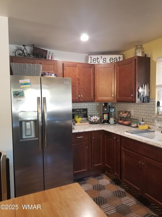 kitchen featuring decorative backsplash, a sink, stainless steel fridge with ice dispenser, and light stone countertops