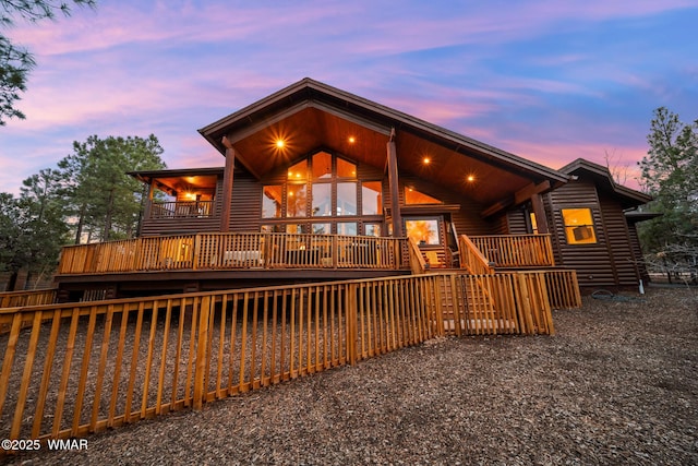 back of house at dusk featuring faux log siding and a deck