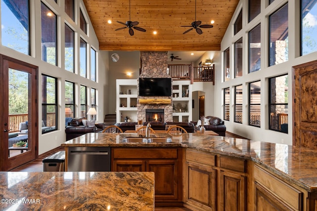 kitchen featuring wooden ceiling, dishwashing machine, brown cabinets, a stone fireplace, and a sink