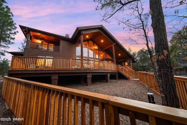 back of property at dusk with log veneer siding, fence, and a balcony