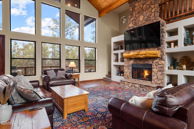 living room with baseboards, wood ceiling, wood finished floors, a stone fireplace, and built in shelves