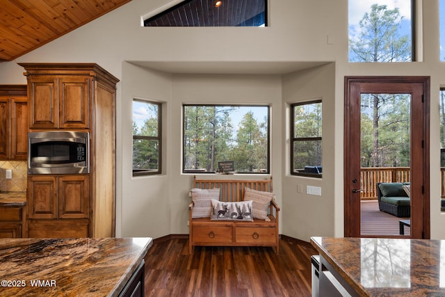 kitchen with visible vents, brown cabinetry, dark countertops, stainless steel microwave, and dark wood-style flooring