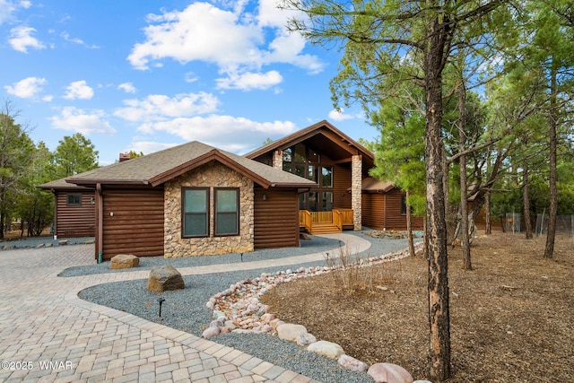 view of front of home with stone siding, faux log siding, decorative driveway, and roof with shingles