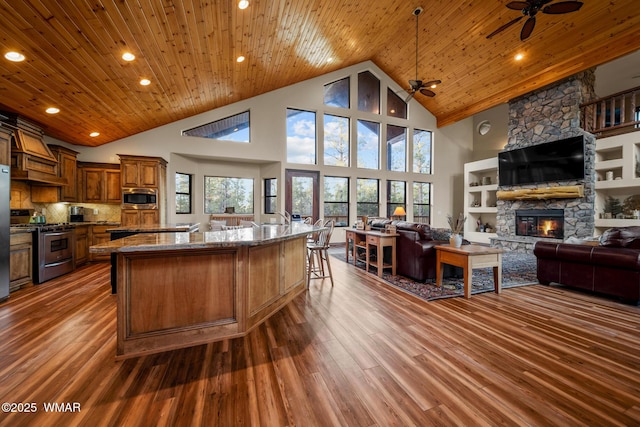 kitchen with wooden ceiling, a fireplace, wood finished floors, appliances with stainless steel finishes, and brown cabinetry