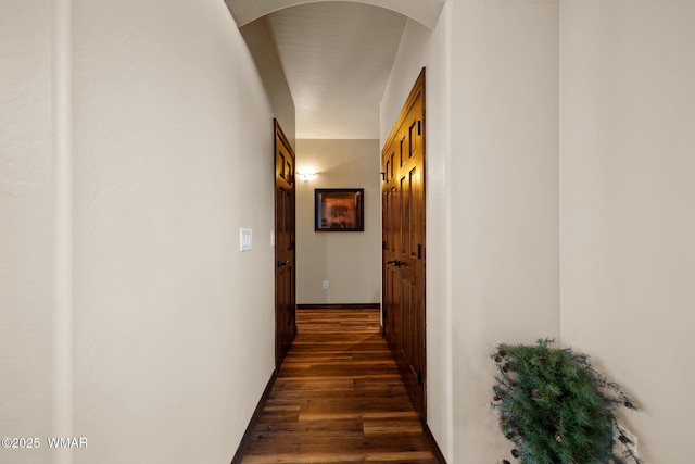 hallway with dark wood-type flooring, arched walkways, and baseboards