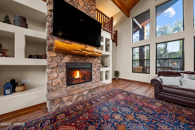 living area featuring high vaulted ceiling, a fireplace, wood finished floors, baseboards, and built in features