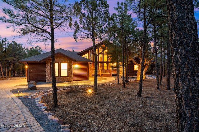 property exterior at dusk with stone siding and a shingled roof