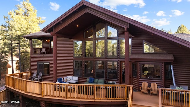 back of house with faux log siding, outdoor lounge area, and a wooden deck