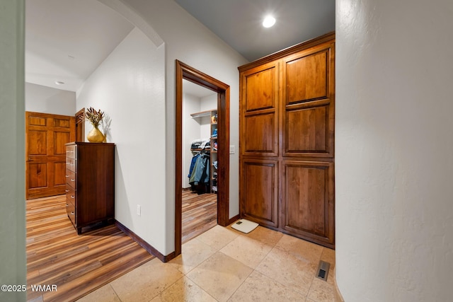 hallway with arched walkways, light wood-type flooring, visible vents, and baseboards