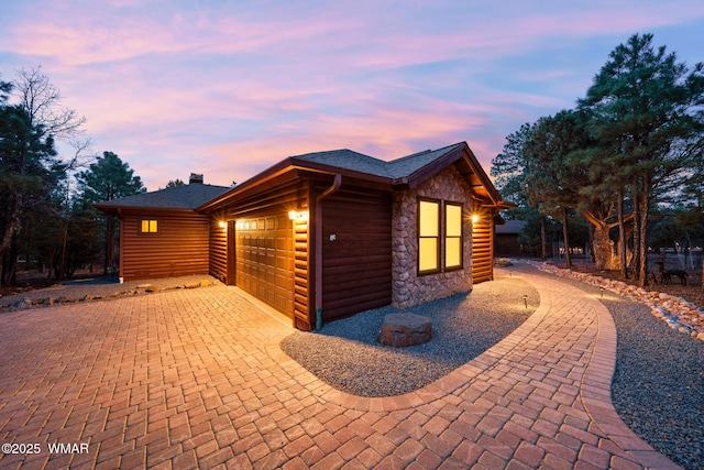 view of property exterior featuring stone siding, decorative driveway, log veneer siding, and an attached garage