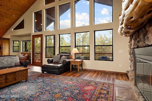 living room with a wealth of natural light, a stone fireplace, baseboards, and wood finished floors