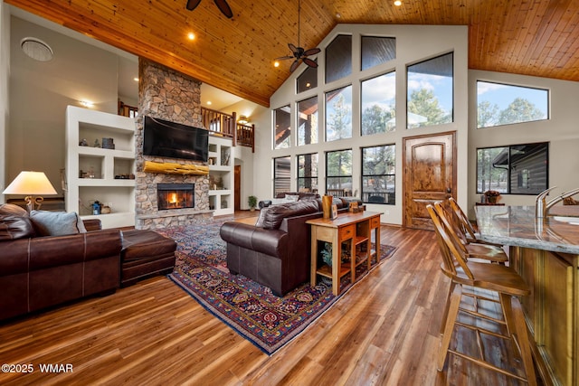 living room with wooden ceiling, ceiling fan, wood finished floors, and a stone fireplace