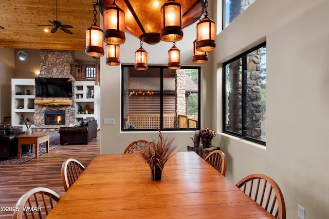 dining room with wood ceiling, ceiling fan, wood finished floors, a high ceiling, and a fireplace