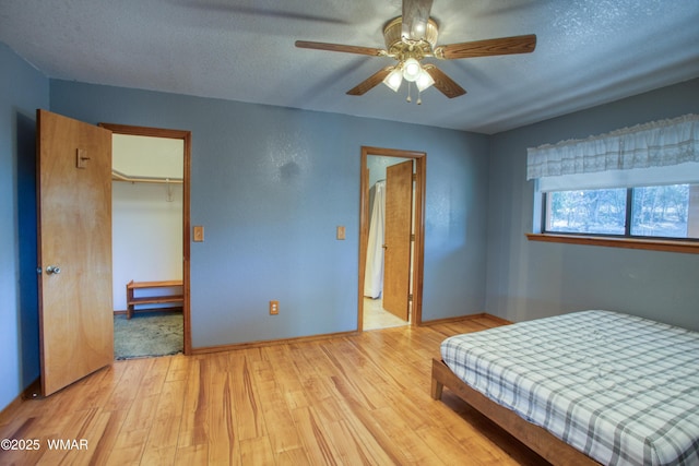 bedroom with light wood-type flooring, a closet, a textured ceiling, a ceiling fan, and baseboards