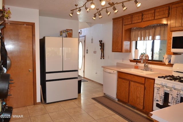 kitchen featuring brown cabinets, white appliances, light countertops, and a sink