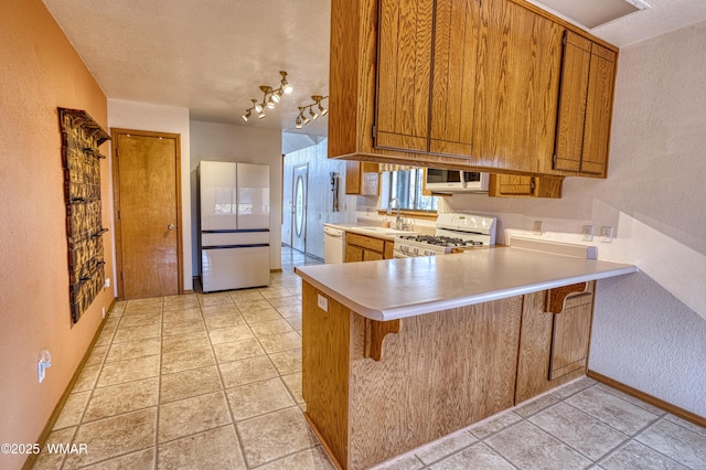 kitchen featuring a sink, light countertops, white appliances, a peninsula, and brown cabinetry