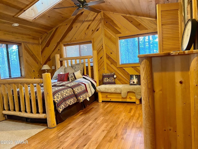 bedroom with vaulted ceiling with skylight, wood ceiling, wood walls, and light wood finished floors