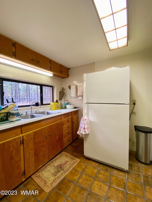 kitchen with brown cabinetry, freestanding refrigerator, light countertops, and a sink