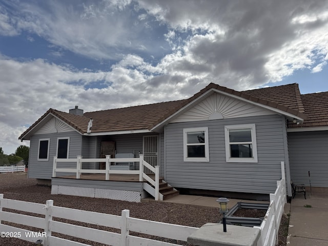 view of front facade featuring a tiled roof, a chimney, fence, and a wooden deck