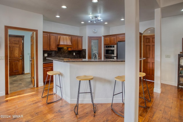 kitchen featuring a breakfast bar, light wood-style floors, dark stone counters, and brown cabinets