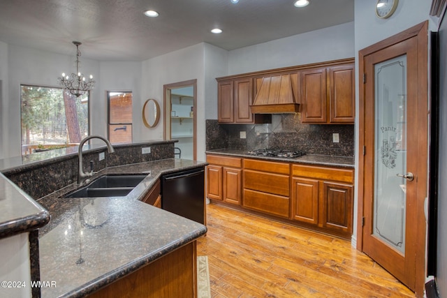 kitchen with a sink, black appliances, brown cabinetry, decorative light fixtures, and custom range hood