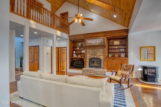 living room featuring a stone fireplace, wooden ceiling, light wood-style flooring, a ceiling fan, and a wood stove